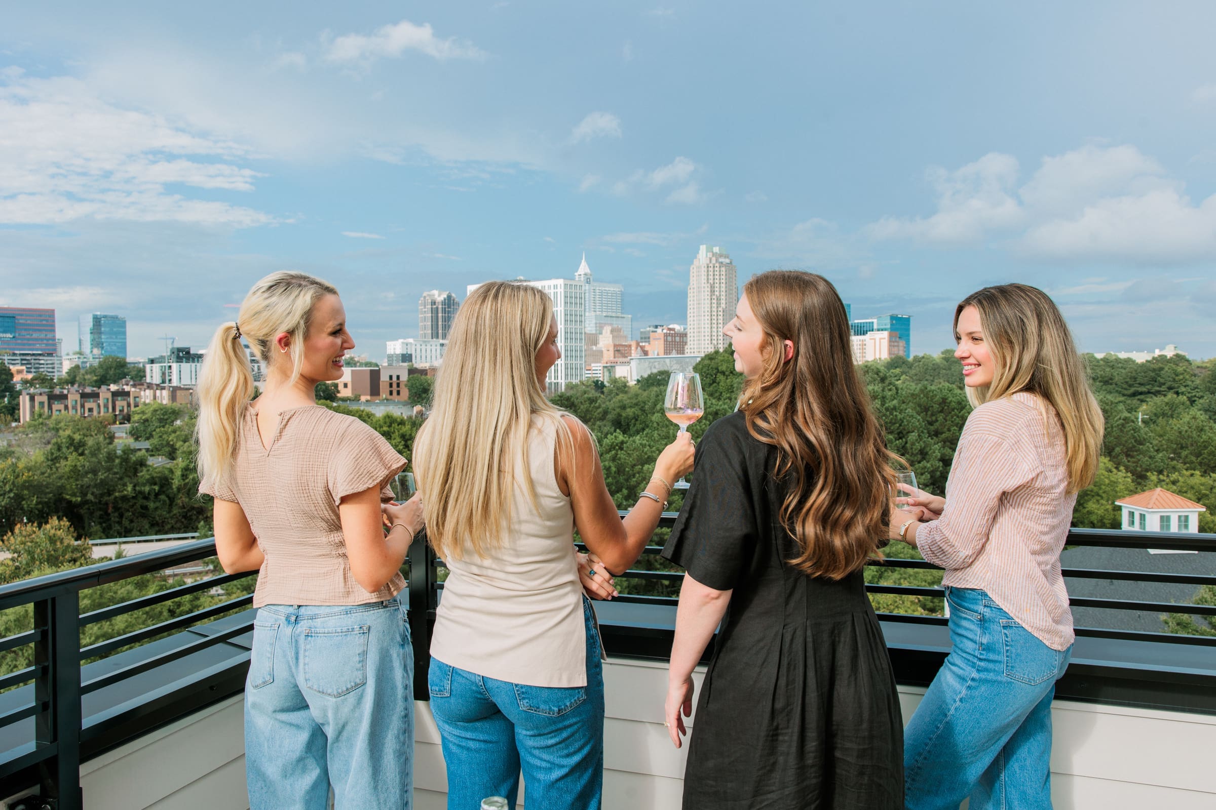 women clinking glasses over view do down town Raleigh skyline on roof top lounge