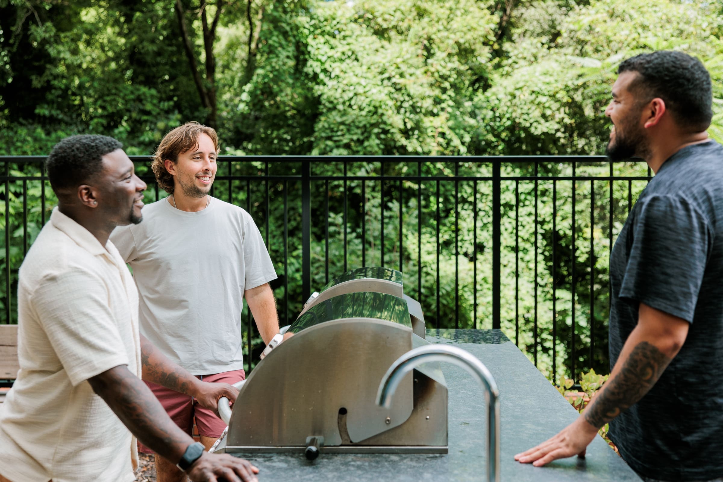3 men talking around grills outside by greenway path